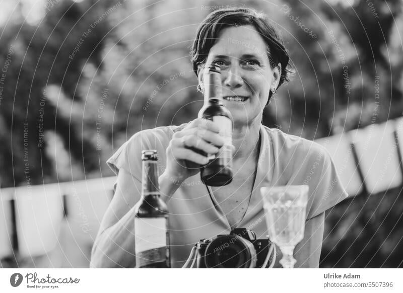 Drinkje bej Inkje | Die Gastgeberin sagt "Prost" - Frau schaut lächelnd in die Kamera und hält eine Flasche Bier hoch Portrait Frauengesicht Kopf Außenaufnahme