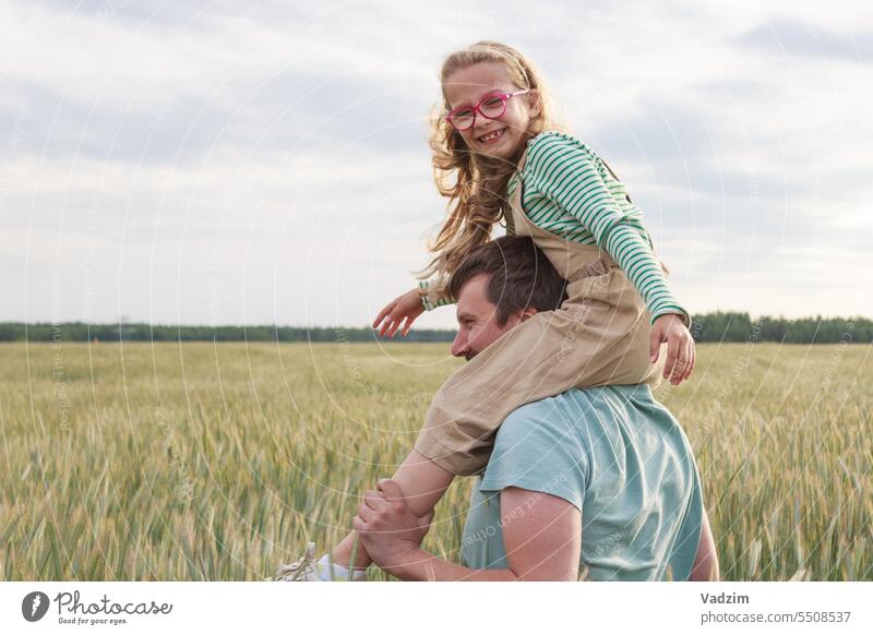 Eine Tochter sitzt auf den Schultern ihres Vaters vor dem Hintergrund eines Weizenfeldes. Glückliche Momente in der Natur. Licht laufen Freude Tag wachsen Ohr