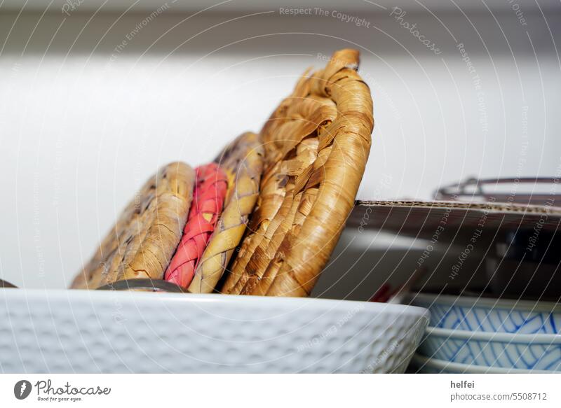 Topfuntersetzer aus Bast im Küchenschrank fotografiert Schrank Farbfoto Häusliches Leben Detailaufnahme hausgemacht Ware Küchengerät Utensil Waren Objekt