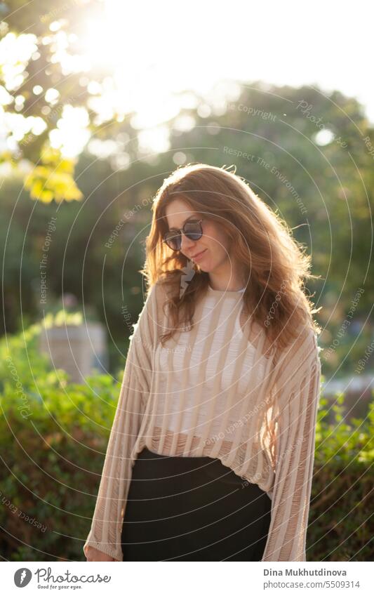 candid Porträt der jungen schönen Frau mit Sonnenbrille im Gegenlicht mit Sonnenlicht im Sommer. Hübsches rothaariges Mädchen mit roten Haaren. Park Lächeln