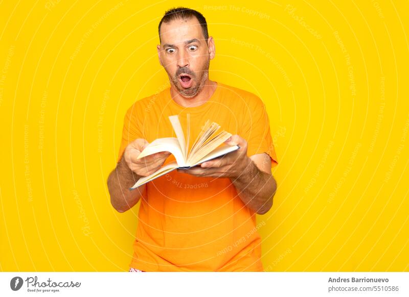 Bärtiger hispanischer Mann in den 40ern blättert sichtlich erregt in einem Buch, isoliert auf gelbem Studiohintergrund. Bildung lernen Notebook klug überrascht