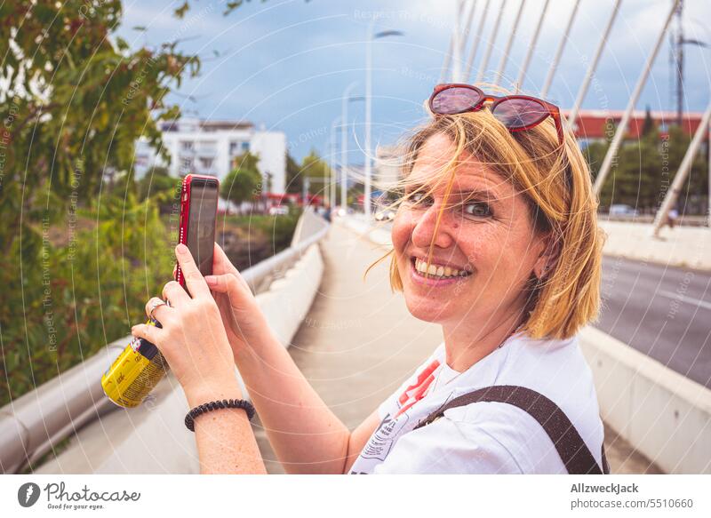 blonde Frau mittleren Alters lächelt in die Kamera beim fotografieren mit dem Handy in Podgorica, Montenegro Porträt Urlaub Urlaubsfoto Urlaubsstimmung Mobile