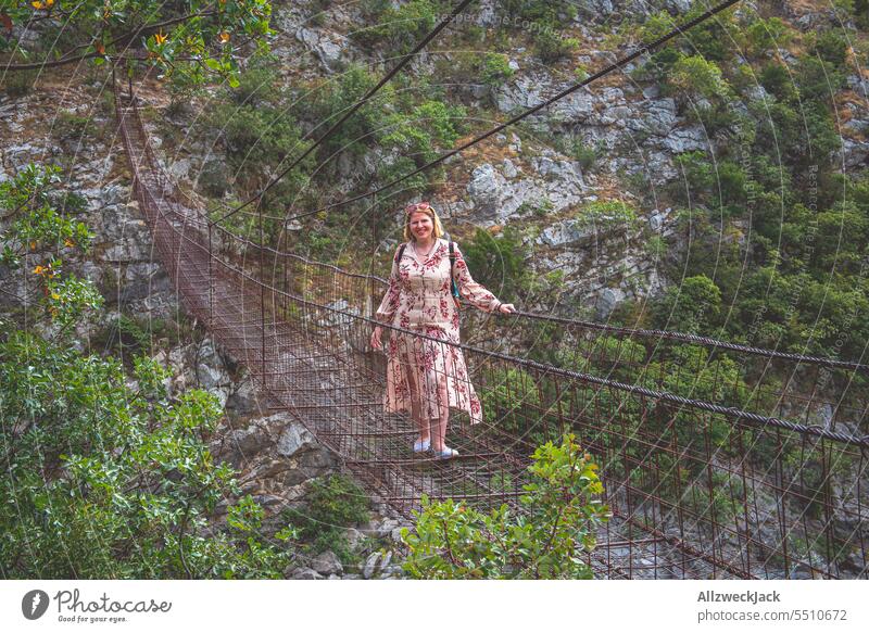 blonde Frau mittleren Alters mit Kleid auf einer alten Hängebrücke in Podgorica, Montenegro blondes Haar Urlaub Urlaubsstimmung wandern Brücke Gefahr gefährlich