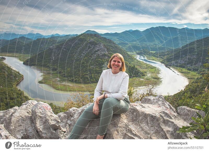blonde Frau mittleren Alters sitzt glücklich vor einem schönen Panorama Ausblick mit Fluss Montenegro Panorama (Aussicht) Tal Aussichtspunkt Flusslauf Natur
