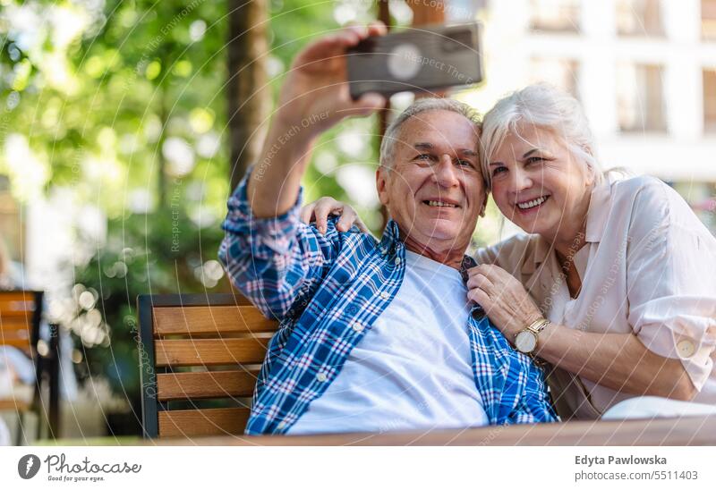 Älteres Paar sitzt am Tisch in einem Café und benutzt ein Mobiltelefon Menschen Stehen Gesundheit Stadtleben graues Haar genießen Straße lässig Tag Porträt
