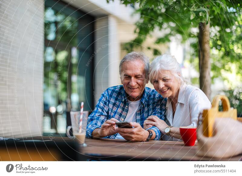 Älteres Paar sitzt am Tisch in einem Café und benutzt ein Mobiltelefon Menschen Stehen Gesundheit Stadtleben graues Haar genießen Straße lässig Tag Porträt