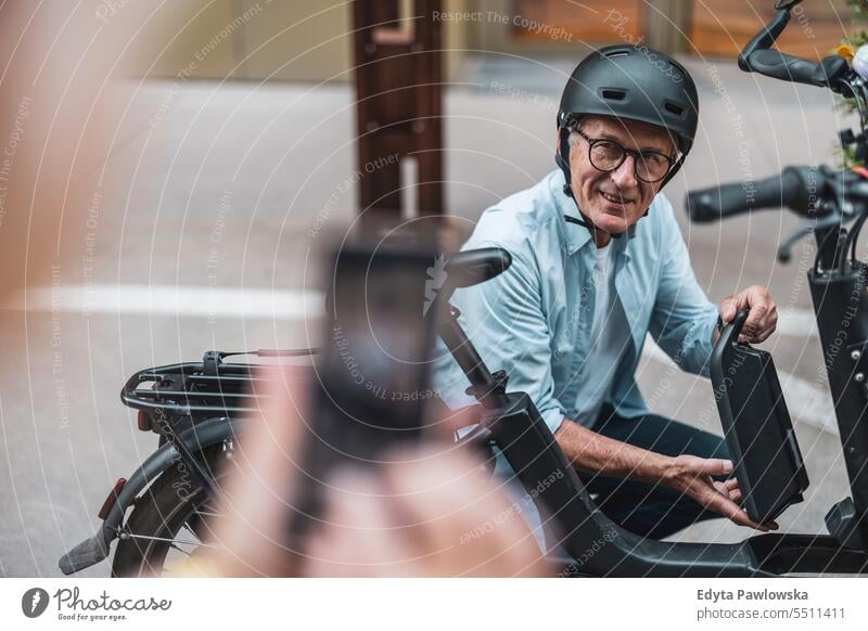 Älterer Mann wechselt die Batterie eines Elektrofahrrads Menschen Kaukasier Stehen Gesundheit Stadtleben graues Haar genießen Straße lässig Tag Porträt