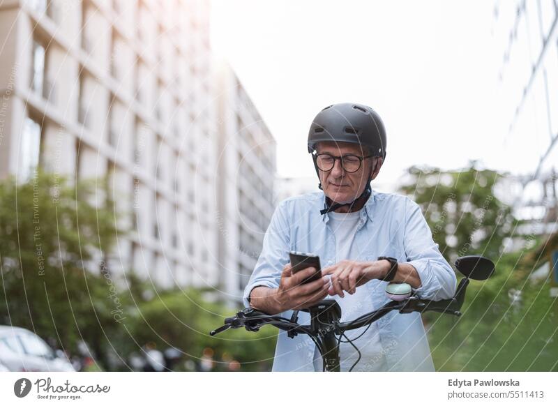 Älterer Mann, der ein Mobiltelefon benutzt, während er in der Stadt Fahrrad fährt Menschen Kaukasier Stehen Gesundheit Stadtleben graues Haar genießen Straße