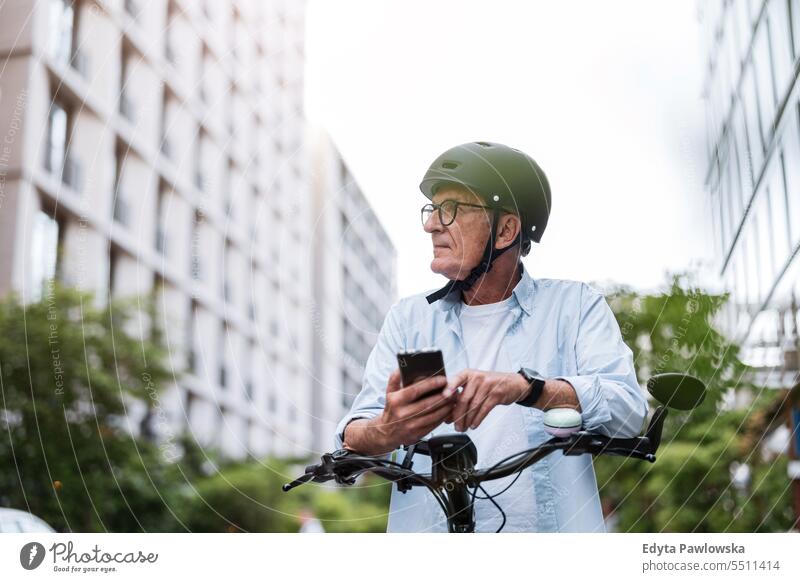 Älterer Mann, der ein Mobiltelefon benutzt, während er in der Stadt Fahrrad fährt Menschen Kaukasier Stehen Gesundheit Stadtleben graues Haar genießen Straße