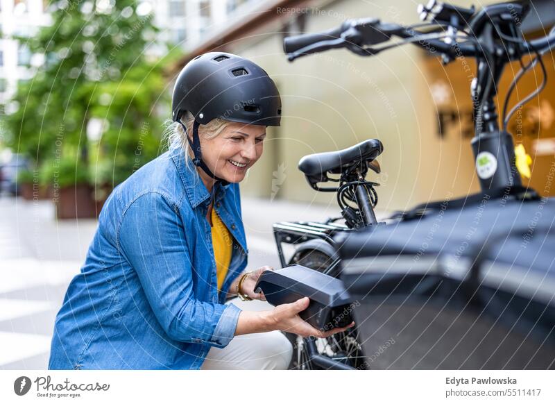 Ältere Frau wechselt die Batterie eines Elektrofahrrads Menschen Kaukasier Stehen Gesundheit Stadtleben graues Haar genießen Straße lässig Tag Porträt außerhalb
