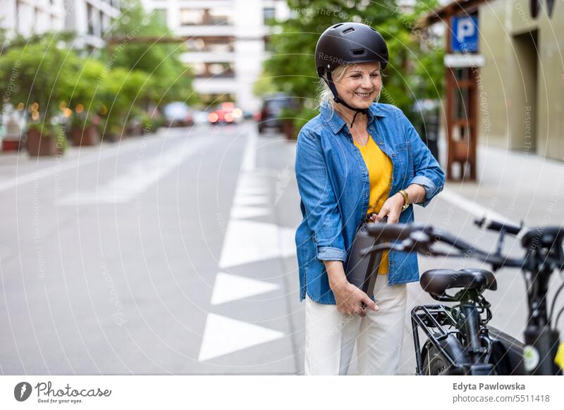 Ältere Frau wechselt die Batterie eines Elektrofahrrads Menschen Kaukasier Stehen Gesundheit Stadtleben graues Haar genießen Straße lässig Tag Porträt außerhalb