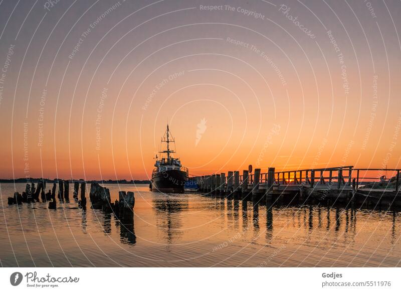 Maritimer Sonnenuntergang. Das Schiff liegt an der Anlegestelle vor Anker. Reflektionen der Holzplanken auf dem Wasser Holzdielen Reflexion & Spiegelung