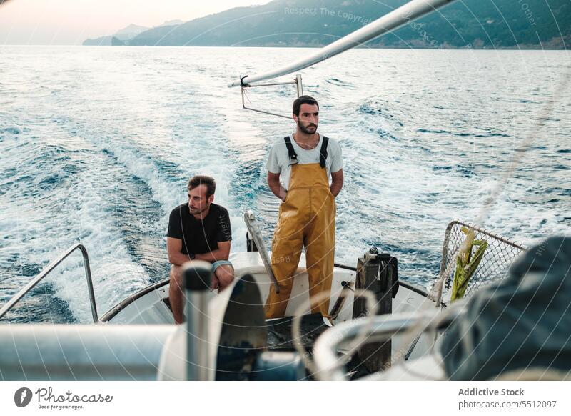 Junge ethnische Fischer fahren auf einem Fischerboot auf plätscherndem Meerwasser Männer reisen Segelboot Berge u. Gebirge Himmel Meereslandschaft Rippeln MEER