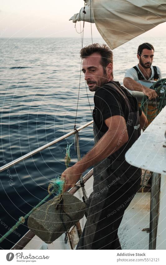 Junge ethnische Männer stehen und ziehen an einem Netz mit Schwimmer auf einem Segelboot Seil MEER Fischen Aktivität Meereslandschaft männlich jung hispanisch