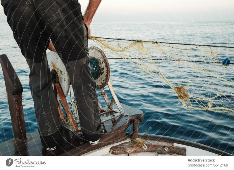 Unbekannter Fischer steht bei Tageslicht in der Nähe des Spiralrades mit Fischernetzfaden Mann Netz Rad Knäuel Gerät Fischen Schuh Seil Spirale Meerwasser