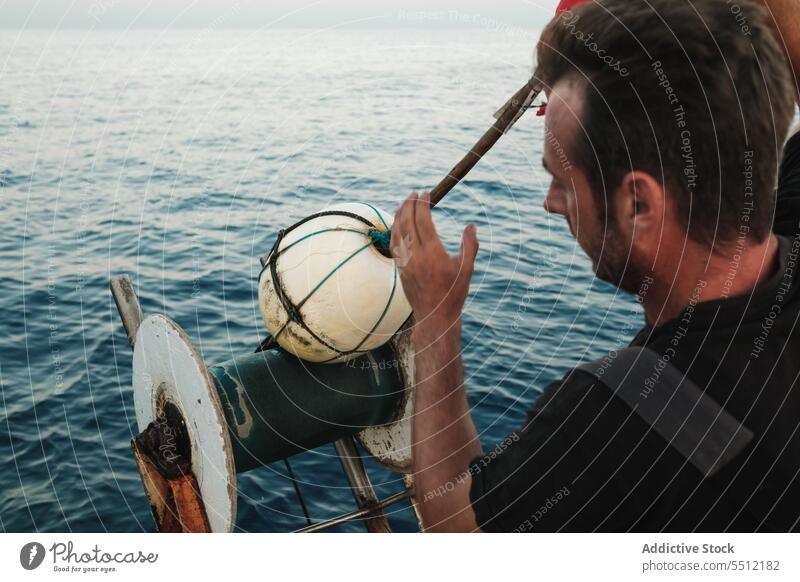 Fokussierter ethnischer Mann, der eine Boje in das plätschernde Meerwasser fallen lässt Windstille MEER Rad Ball Gerät Spirale Kugel männlich jung hispanisch