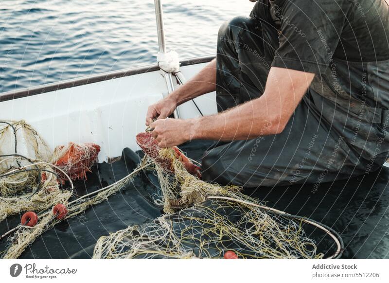 Anonymer Mann, der mit der Hand die Fäden des Fischernetzes entwirrt, um bei Tageslicht Fische zu fangen Netz Fischen Boot Wasser Schiffsdeck Gerät Natur