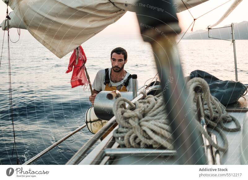 Fokussierter junger ethnischer Mann mit Flagge und Boje auf einem Segelboot im Tageslicht stehend Boot Fahne Lebensretter Meereslandschaft reisen Ausflug Natur