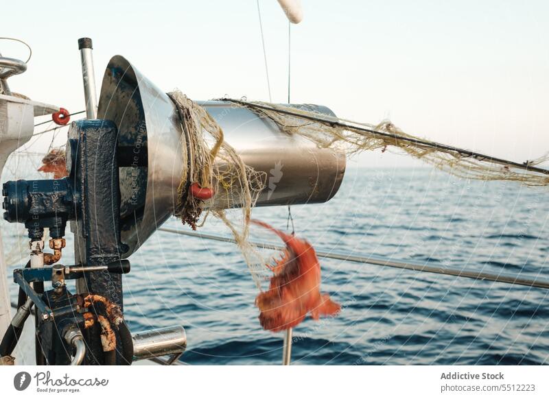 Fischernetz auf runder Trommel eines Bootes auf plätscherndem Meerwasser mit hängenden roten Garnelen Fischen Netz marin Natur Rippeln Seil Granele gebunden