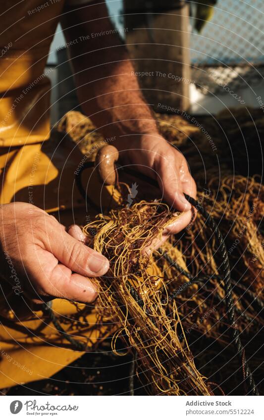 Anonymer Mann, der mit der Hand die Fäden des Fischernetzes entwirrt, um bei Tageslicht Fische zu fangen Netz Fischen Boot Wasser Schiffsdeck Gerät Natur