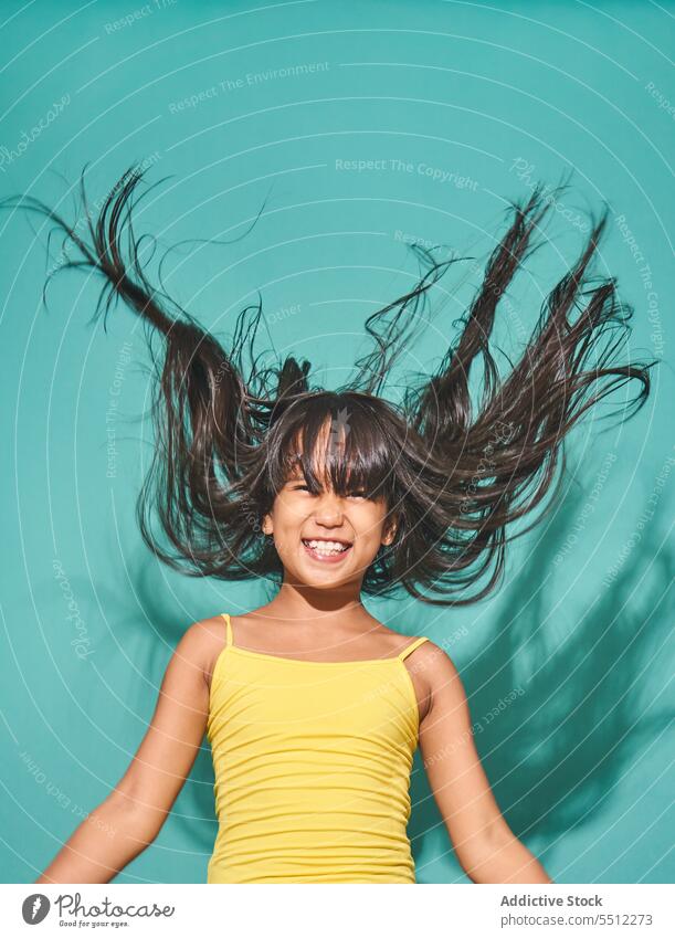 Glückliches ethnisches Mädchen, das vor einem türkisfarbenen Hintergrund steht Lächeln Kind niedlich positiv Freude asiatisch Kindheit heiter bezaubernd Frieden