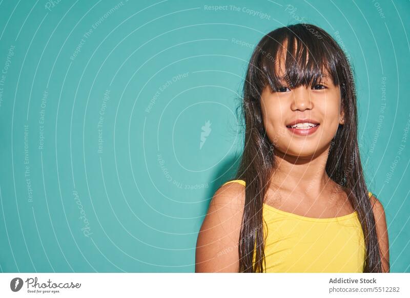 Glückliches ethnisches Mädchen, das vor einem türkisfarbenen Hintergrund steht Porträt Lächeln Kind niedlich positiv Freude asiatisch Kindheit heiter bezaubernd