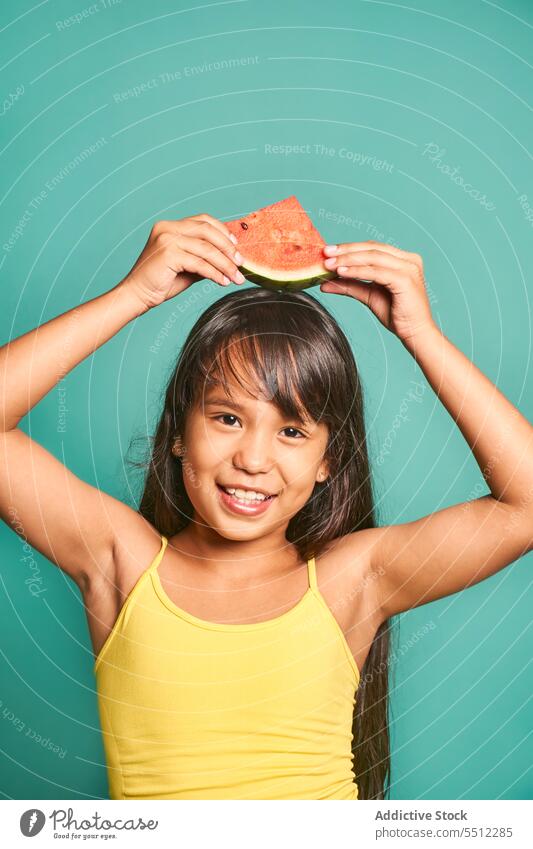 Glückliches ethnisches Mädchen mit einem Stück Wassermelone vor türkisfarbenem Hintergrund Kind Porträt Kindheit zeigen niedlich lecker spielerisch asiatisch