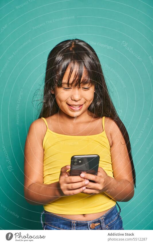 Lustige ethnische Mädchen Kind stehend mit Smartphone in der Nähe von türkisfarbenen Hintergrund lustig benutzend niedlich Lächeln heiter asiatisch Mobile