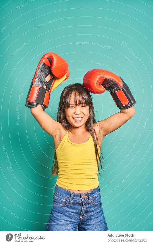 Fröhliches ethnisches Mädchen mit Boxhandschuhen vor türkisfarbenem Hintergrund Kind Lächeln Boxsport Handschuh Porträt froh positiv heiter Raum spielerisch
