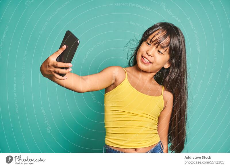 Lustige ethnischen Mädchen Kind stehend mit Smartphone und unter Selfie in der Nähe von türkisfarbenen Hintergrund lustig benutzend niedlich Lächeln heiter