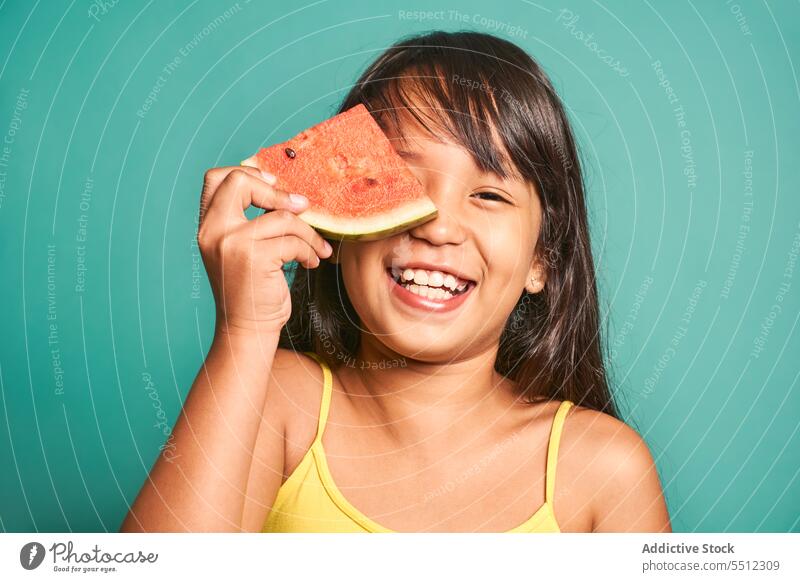Happy ethnischen Mädchen Kind stehend Stück Wassermelone in der Nähe von Gesicht gegen türkisfarbenen Hintergrund süß niedlich lecker Lächeln bezaubernd