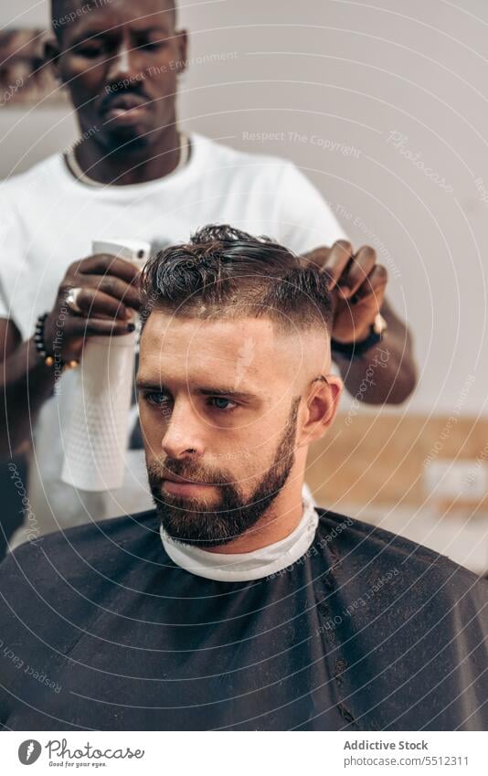 Schwarzer Friseur sprüht Wasser auf das Haar eines Kunden Männer Klient Haarschnitt Salon Barbershop Spray Behaarung Sprühgerät maskulin Konzentration jung
