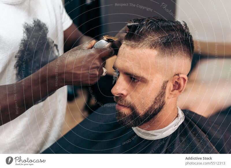 Mann bekommt professionellen Haarschnitt im Friseursalon Männer Klient entgittern Behaarung Trimmer Barbershop maskulin jung männlich rassenübergreifend