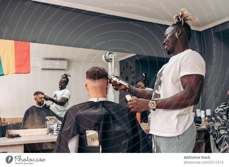 Fröhlicher Friseur, der das Haar eines männlichen Kunden schneidet Männer Klient Haarschnitt entgittern Behaarung Trimmer Barbershop Genauigkeit Schönheit jung