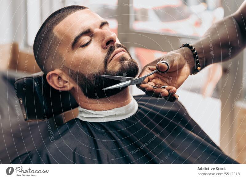 Schwarzer Barbier schneidet Bart eines Kunden mit einer Schere Männer Friseur Klient geschnitten Vollbart brutal Schönheit Behaarung Barbershop jung männlich