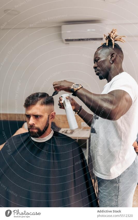 Schwarzer Friseur sprüht Wasser auf das Haar eines Kunden Männer Klient Haarschnitt Salon Barbershop Spray Behaarung Sprühgerät maskulin Konzentration jung