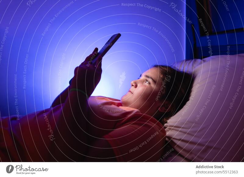 Verängstigtes junges Mädchen, das mit seinem Smartphone auf dem Bett liegt und auf den Bildschirm schaut Film beängstigend zuschauen Teenager erschrecken