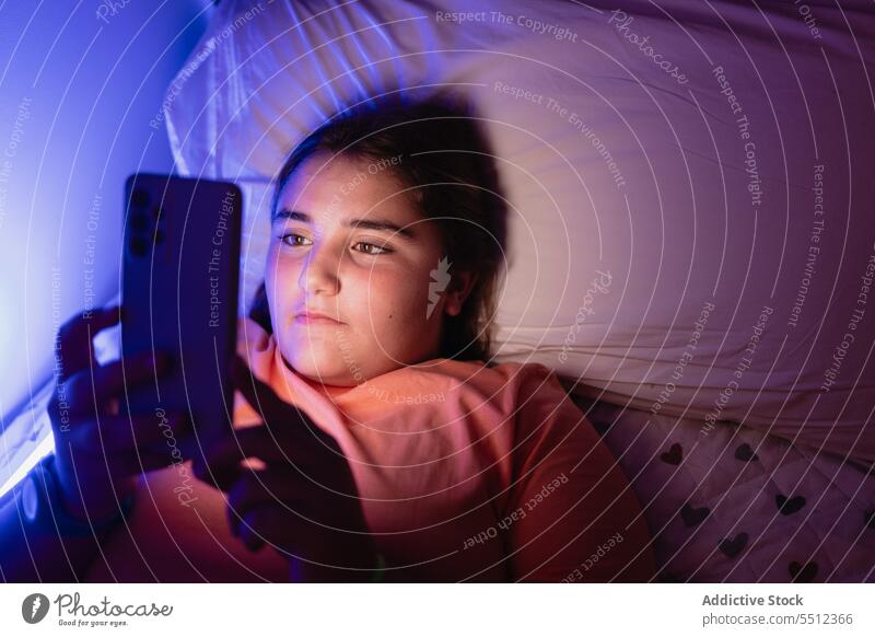 Positives junges Mädchen, das mit seinem Smartphone auf dem Bett liegend auf den Bildschirm schaut Film beängstigend zuschauen Teenager erschrecken ernst