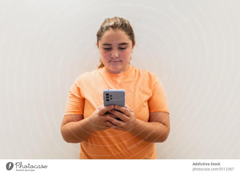 Ernstes junges Mädchen steht mit Smartphone in der Nähe der grauen Wand Teenager selbstbewusst benutzend Vorschein ernst Kommunizieren Anschluss T-Shirt Hülse