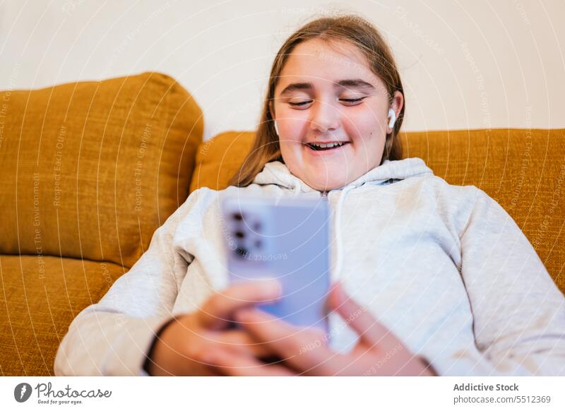 Fröhliches junges Mädchen am Smartphone auf dem Sofa sitzend Videoanruf Lächeln online benutzend Kommunizieren Anschluss Internet Teenager Apparatur Gerät