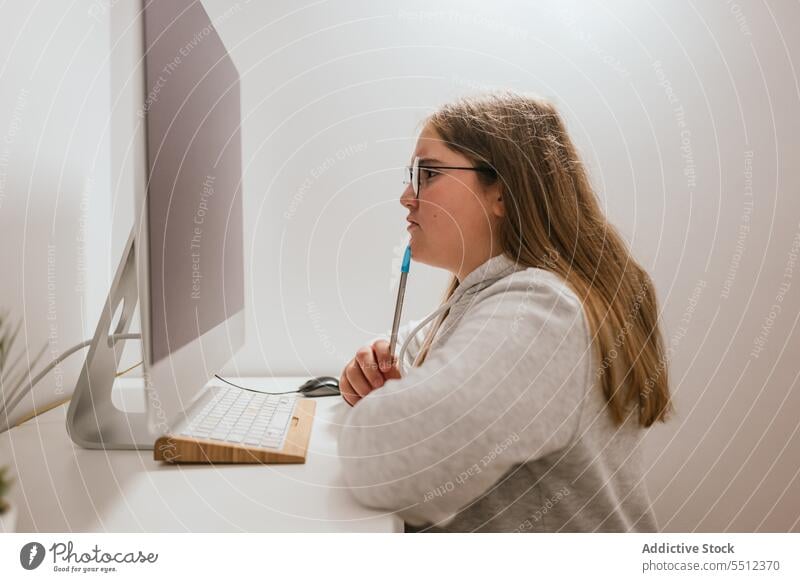 Ernstes Mädchen sitzt am Tisch mit Stift und schaut auf den Monitor zu Hause Computer eingetopft Pflanze Schreibtisch hell Licht Teenager Fokus Laptop Apparatur