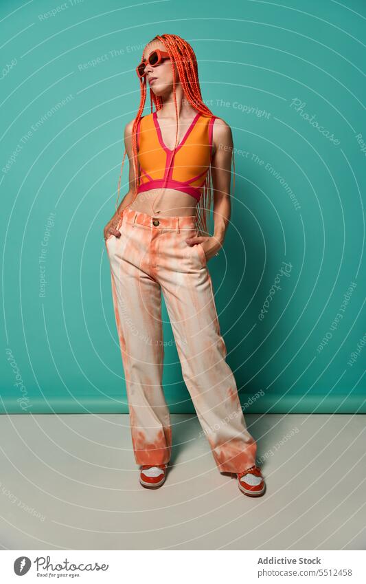 Stylische Frau in orangefarbenem Outfit und Sonnenbrille selbstbewusst stylisch Mode Model Studioaufnahme emotionslos cool lebhaft Vorschein jung Afro-Zöpfe Top