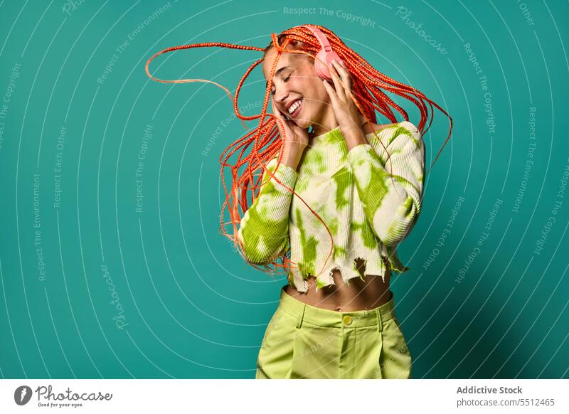 Fröhliche Frau mit Afrozöpfen, die über Kopfhörer Musik hört zuhören Tanzen pulsierend springen Porträt meloman stylisch Studioaufnahme Energie aufgeregt Glück