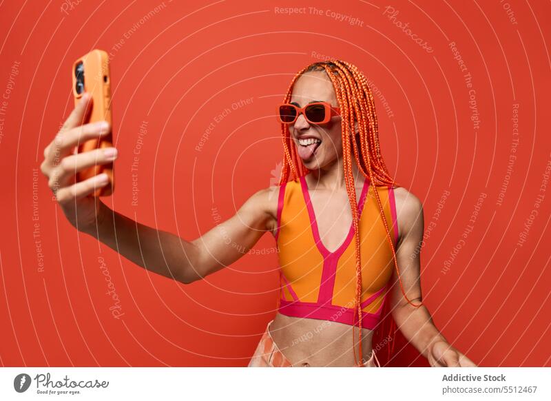 Fröhlicher weiblicher Hipster zeigt Zunge beim Selfie machen Frau benutzend Smartphone Zunge zeigen fotografieren Studioaufnahme soziale Netzwerke charismatisch