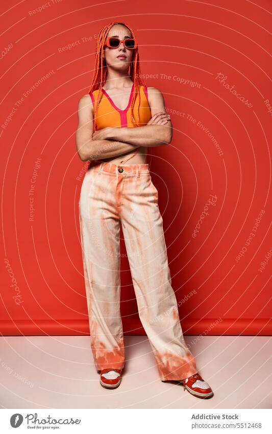 Stylische Frau in orangefarbenem Outfit und Sonnenbrille selbstbewusst stylisch Mode Model Studioaufnahme emotionslos cool lebhaft Vorschein jung Afro-Zöpfe Top