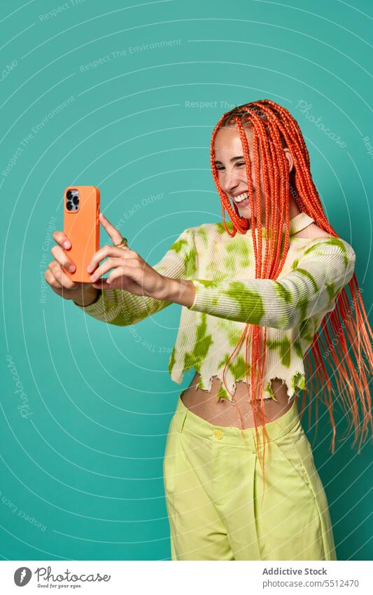 Stilvolle glückliche Frau mit Afrozöpfen, die ein Selfie mit ihrem Smartphone macht benutzend heiter Lächeln fotografieren stylisch Glück Studioaufnahme Model