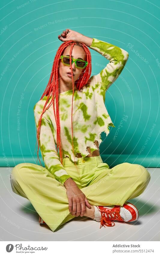 Trendy Frau in stilvollem Outfit sitzt mit gekreuzten Beinen selbstbewusst stylisch Mode Hand auf Kopf Beine gekreuzt Model Studioaufnahme cool lebhaft