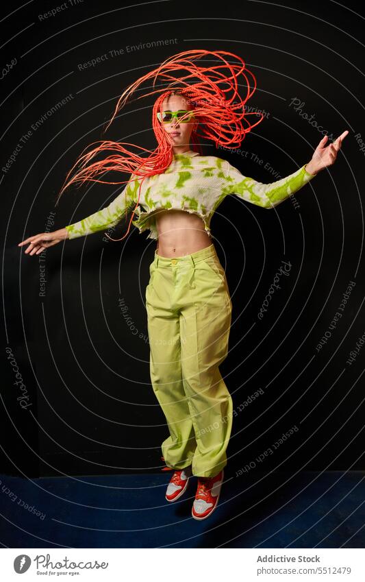 Trendy Frau springt in dunklem Studio Hipster springen stylisch Energie modern Model Studioaufnahme cool fliegendes Haar jung Afro-Zöpfe Sonnenbrille Langarm