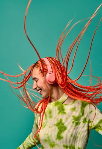 Fröhliche Frau mit Afrozöpfen, die über Kopfhörer Musik hört zuhören Tanzen pulsierend Porträt meloman stylisch Studioaufnahme Energie aufgeregt Glück genießen
