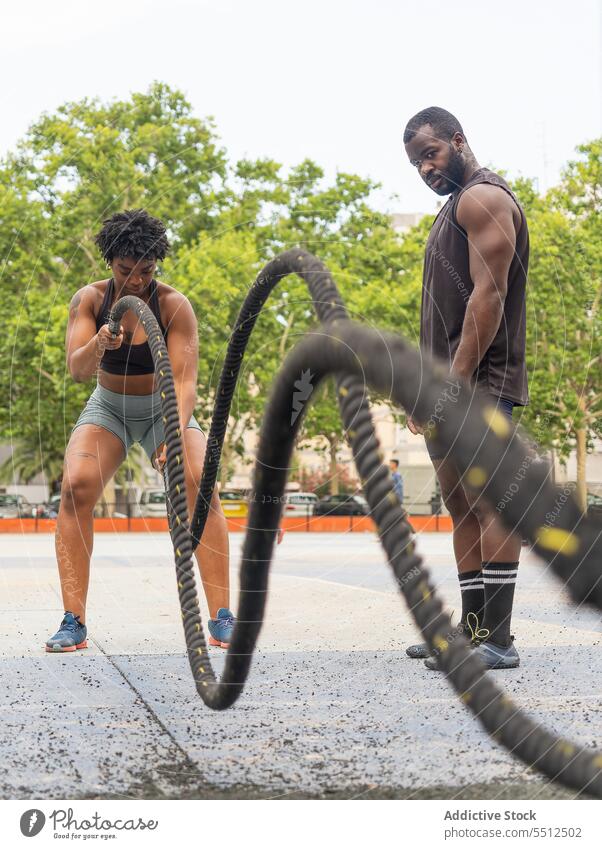 Schwarze Sportlerin bei einer Übung mit Kampfseilen Frau Mann Ausbilderin Trainerin Athlet Bestimmen Sie Training Erwachsener operativ schwarz Afroamerikaner